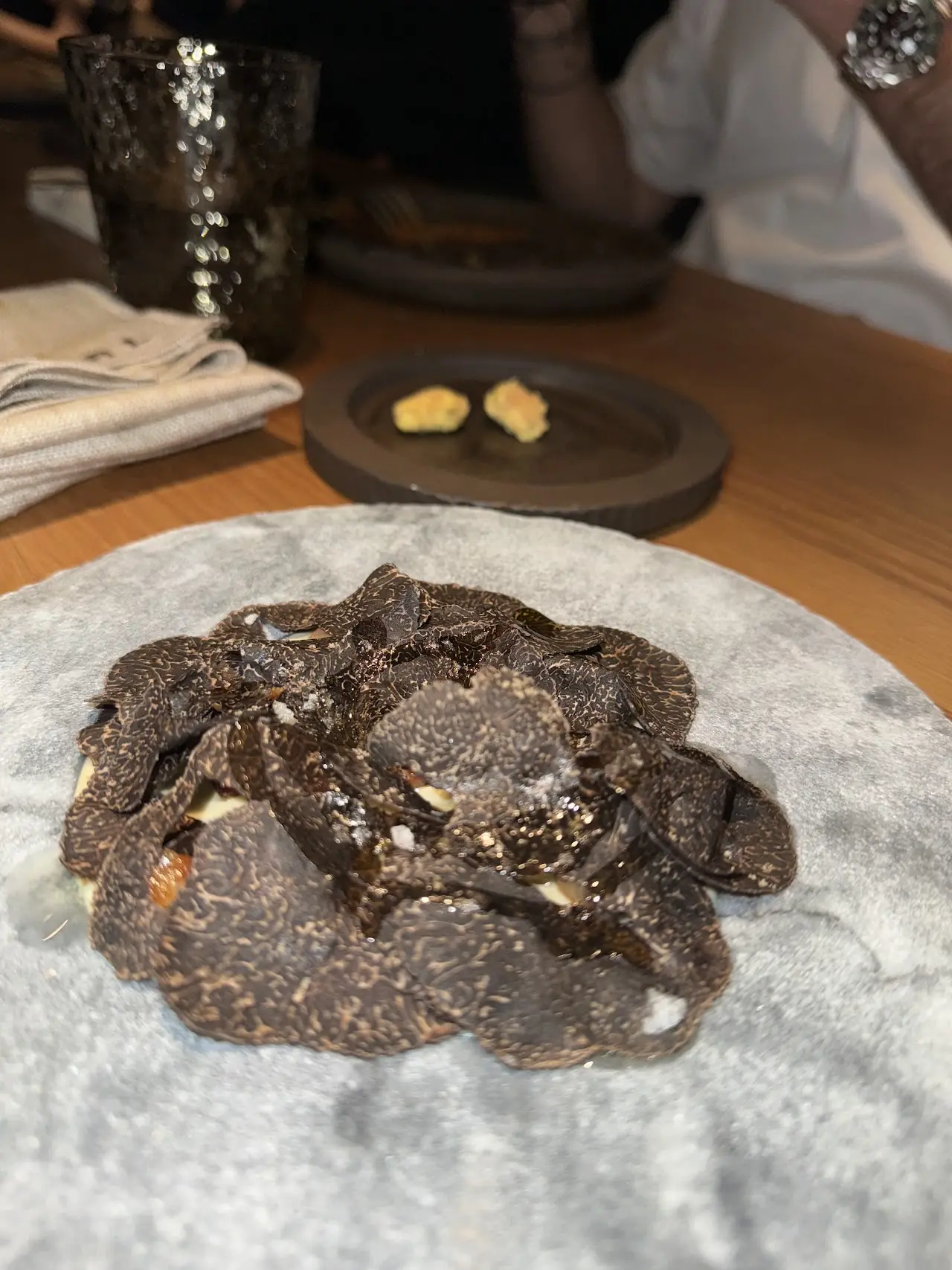 Shaved black truffle piled on a plate lined with a white cloth.