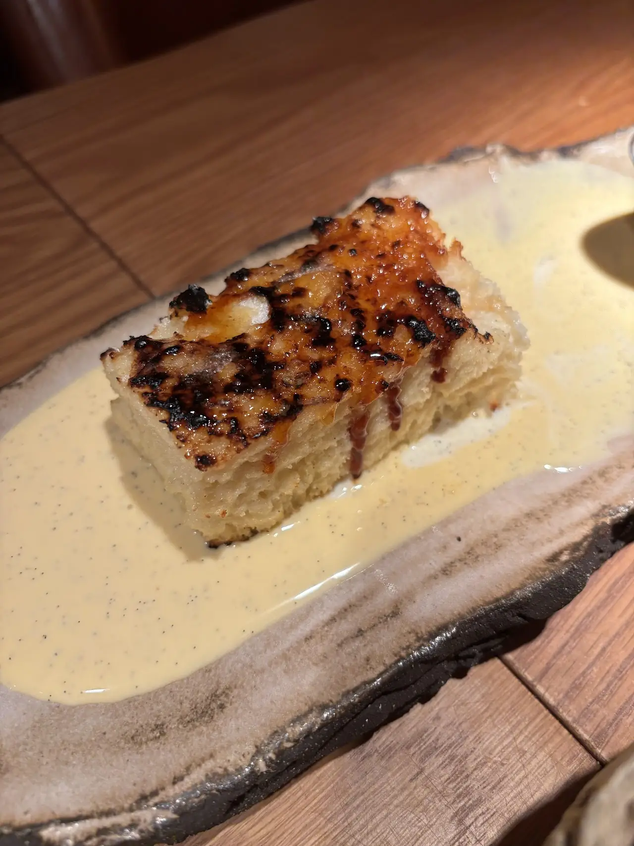 A grilled dish with a caramelized top, served in a pool of cream sauce on a rustic board.