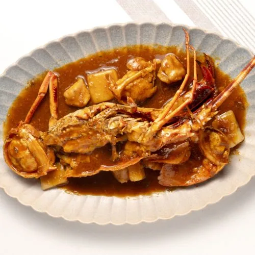 Fluted oval dish of lobster halves braised with chunks of chicken and potato in a thick brown sauce with dried red peppers
