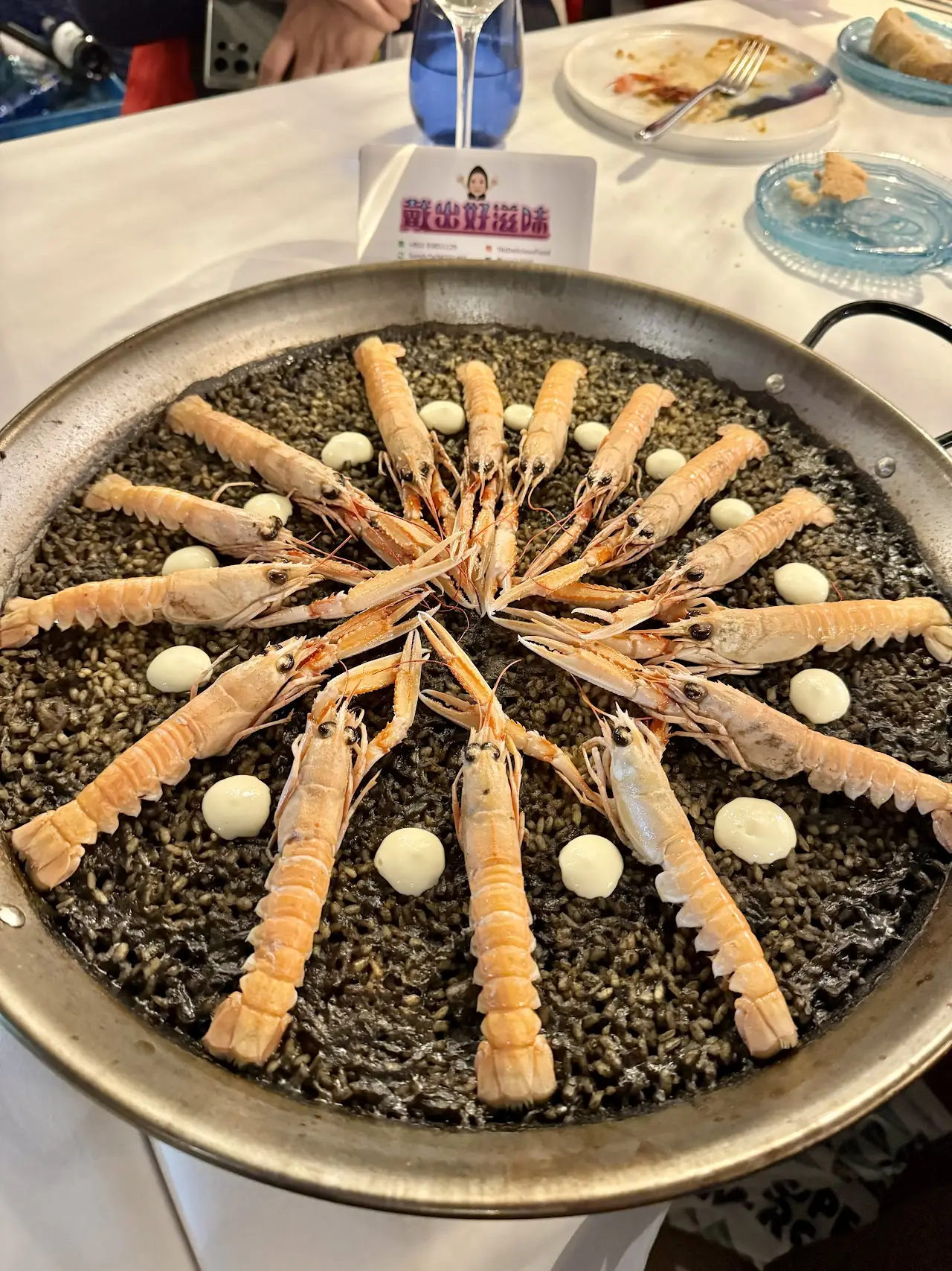 A pan of black rice with seafood arranged in a ring and dots of aioli