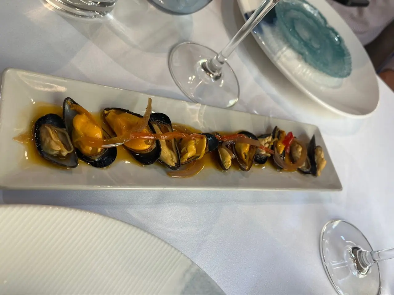 Mussels on the half shell in a sauce, arranged on a long rectangular plate