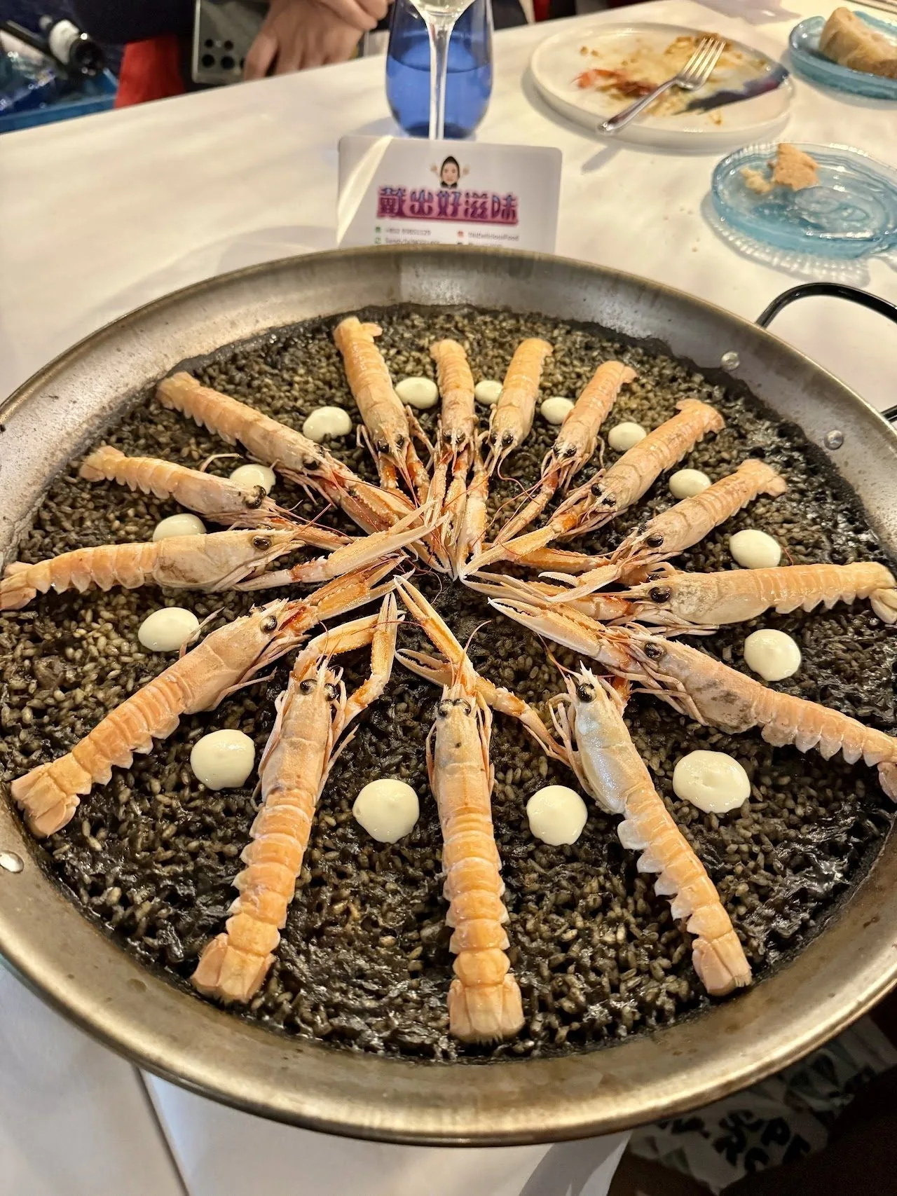 A large pan of dark rice topped with a ring of long razor-shaped shellfish