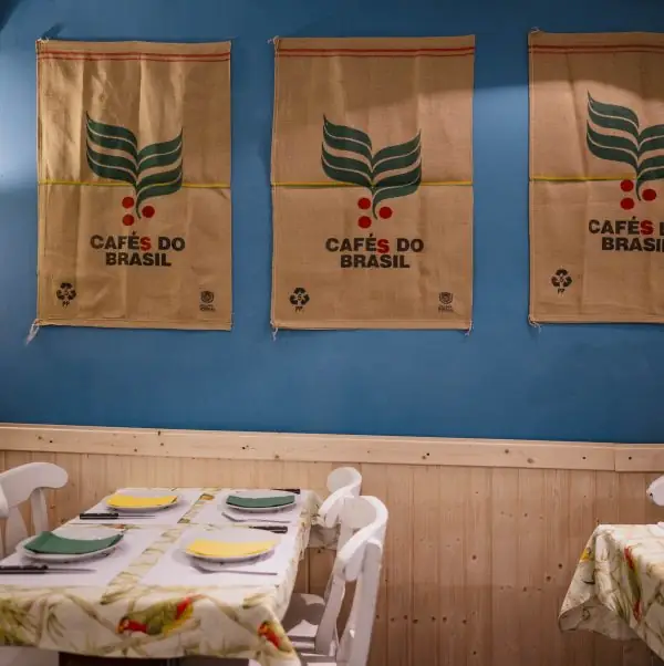 Restaurant interior with a set table below a blue wall hung with three 'Cafes do Brasil' burlap coffee sacks