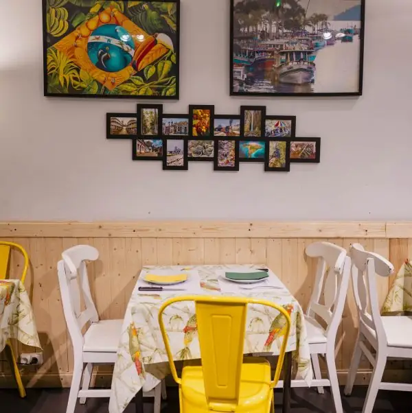 Restaurant corner with a set table, white and yellow chairs, and framed Brazilian artwork and photo collage on the wall