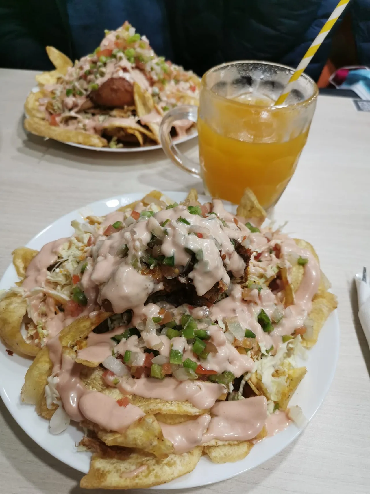 A plate of loaded fries topped with meat, cheese and pico de gallo, with a mango juice