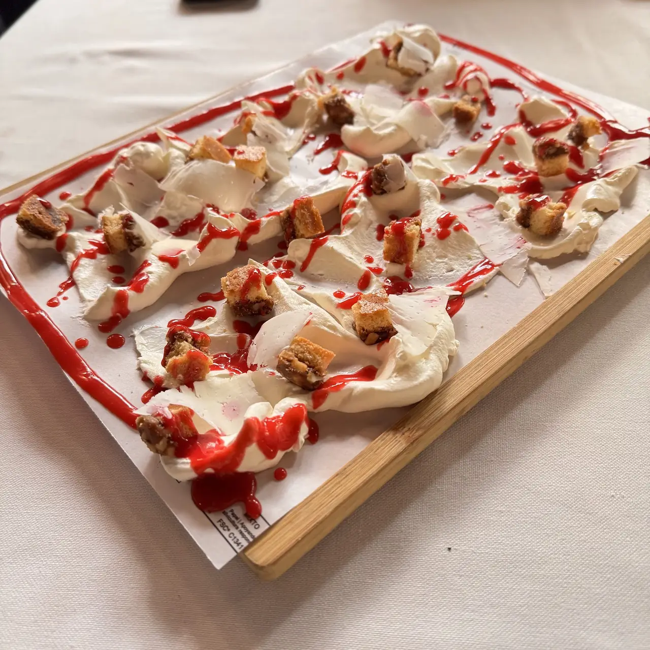 Deconstructed dessert with whipped cream, cake pieces and red berry sauce on a wooden board