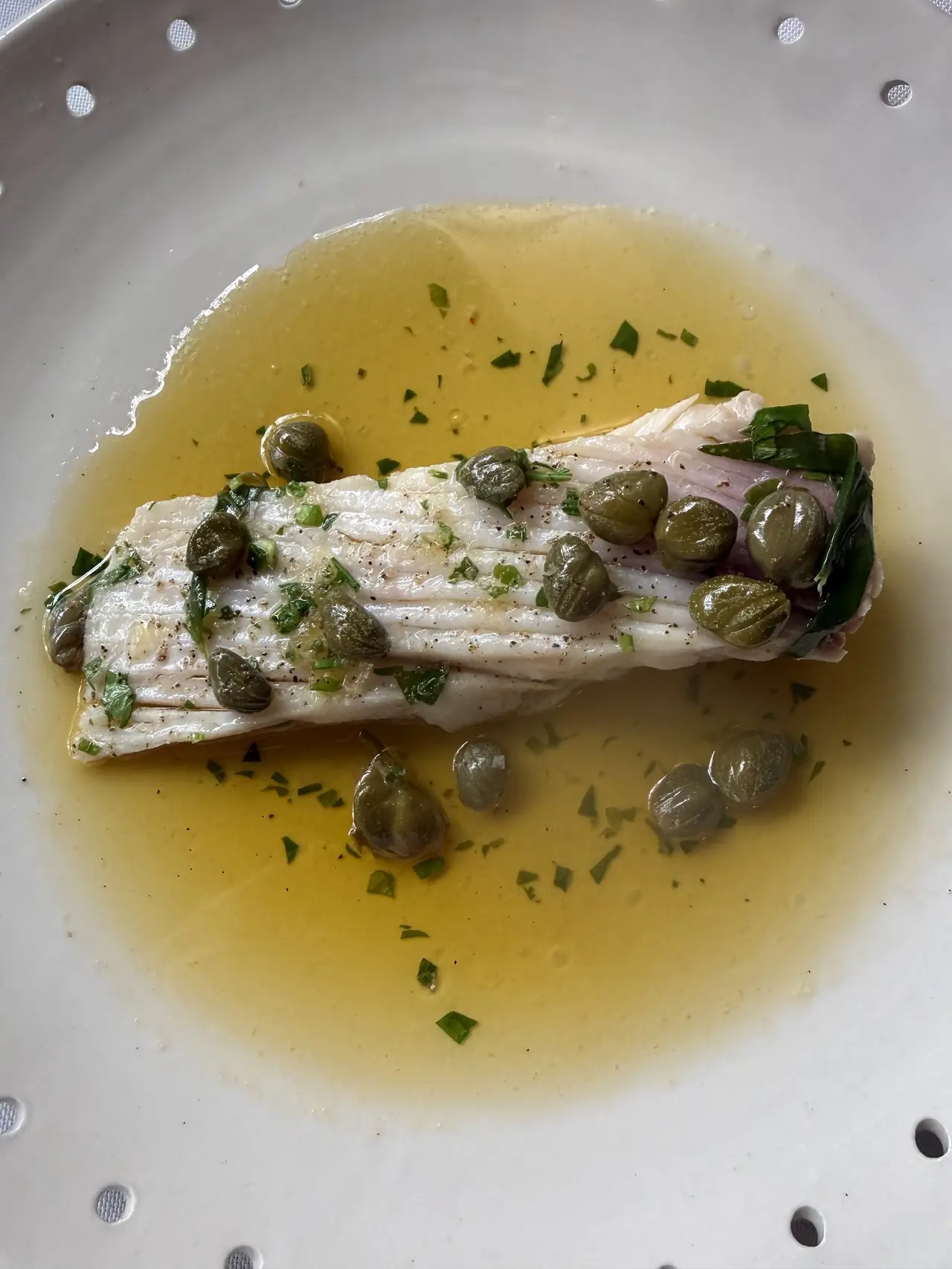 White fish fillet with capers and herbs in olive oil sauce on a plate