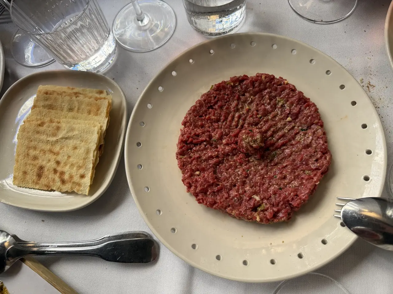 Beef tartare shaped into a disc on a plate, served with crisp flatbread