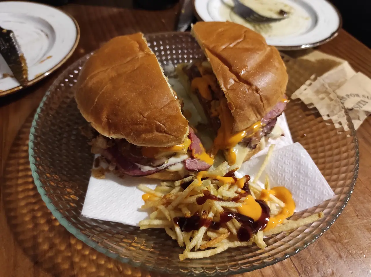 Sliced sandwich with meat and melted cheese, halved, with matchstick fries drizzled in sauce