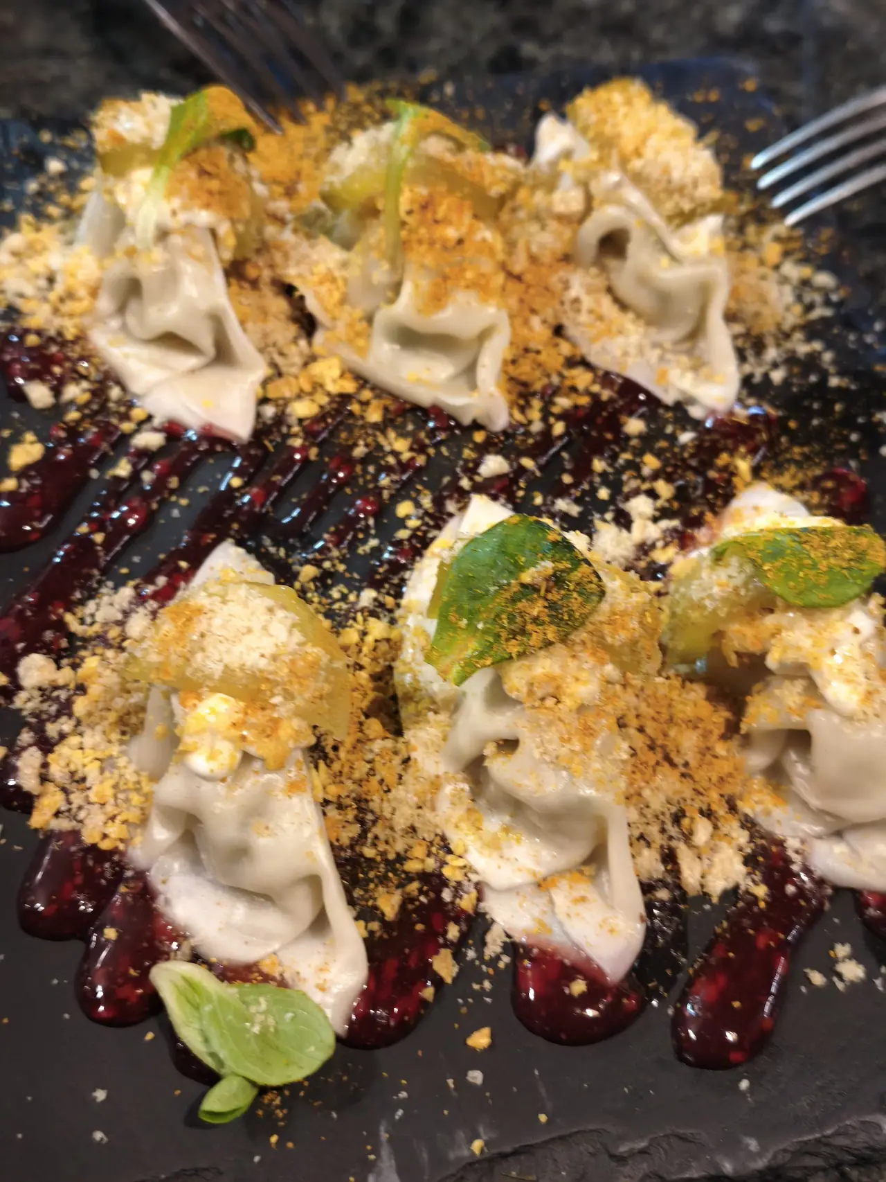 Gyozas on a slate with a dark berry sauce, crumbs and leaves