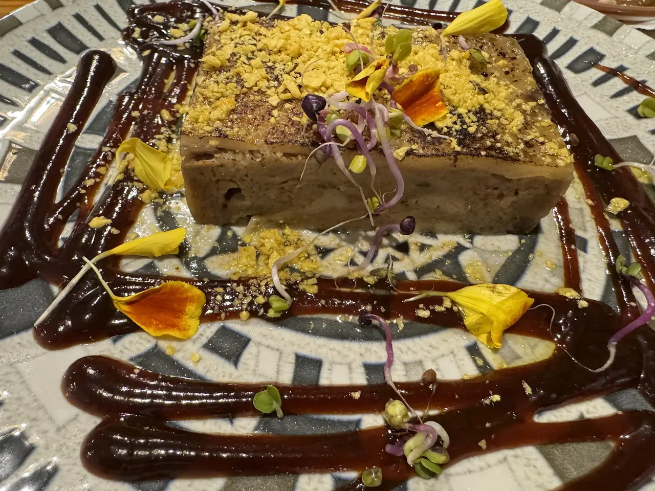 Terrine block topped with crumb and edible flowers, sauce swirled around plate