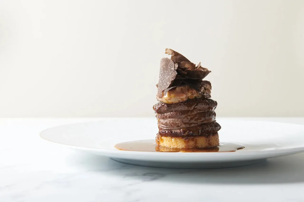 A tall stacked meat dish with a dark glaze on a white plate