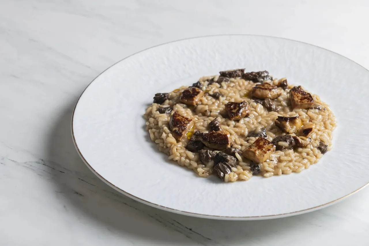 A round white plate of risotto with mushrooms on a marble surface