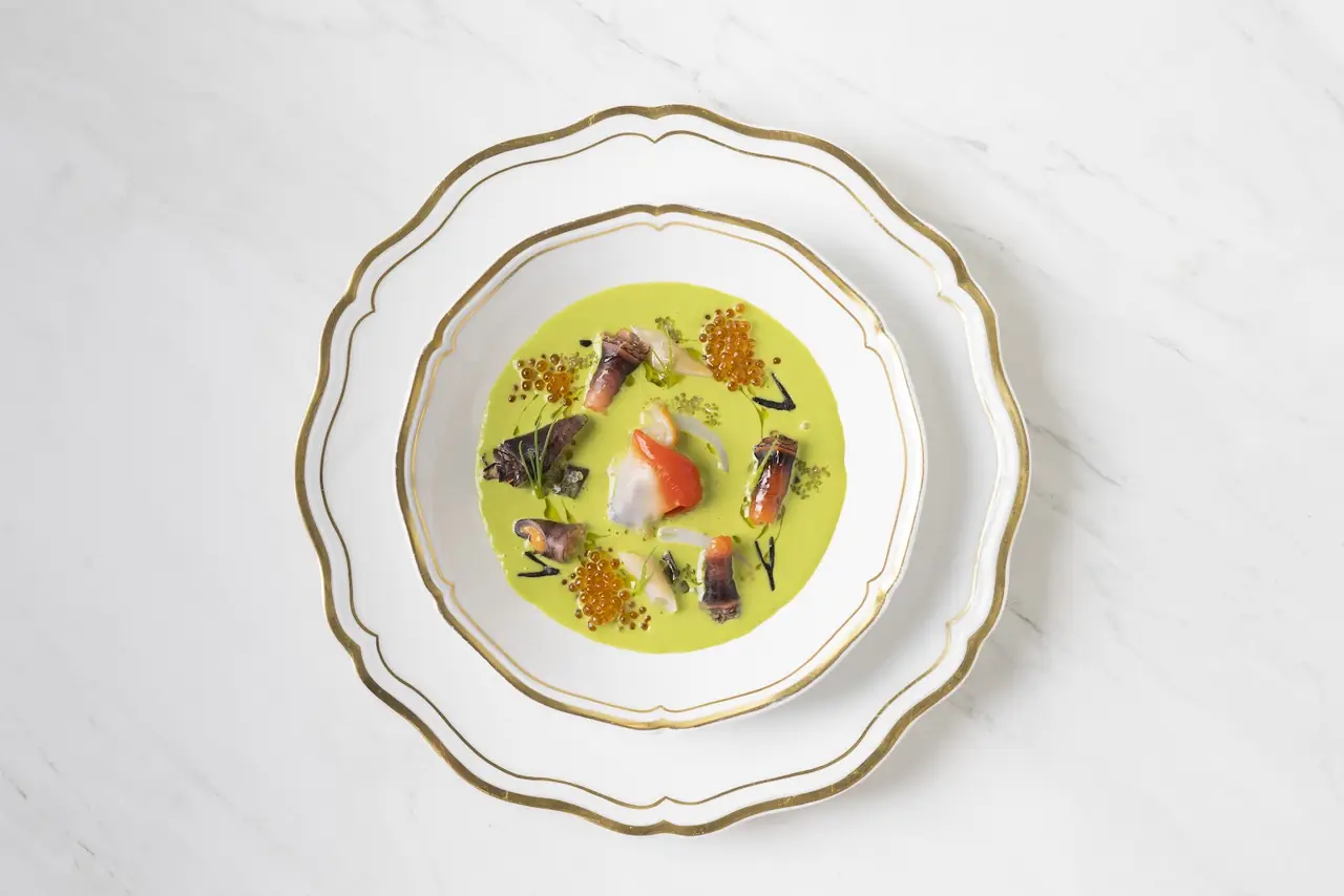 Plated dish with green sauce, seafood pieces, orange roe, on gold-rimmed china