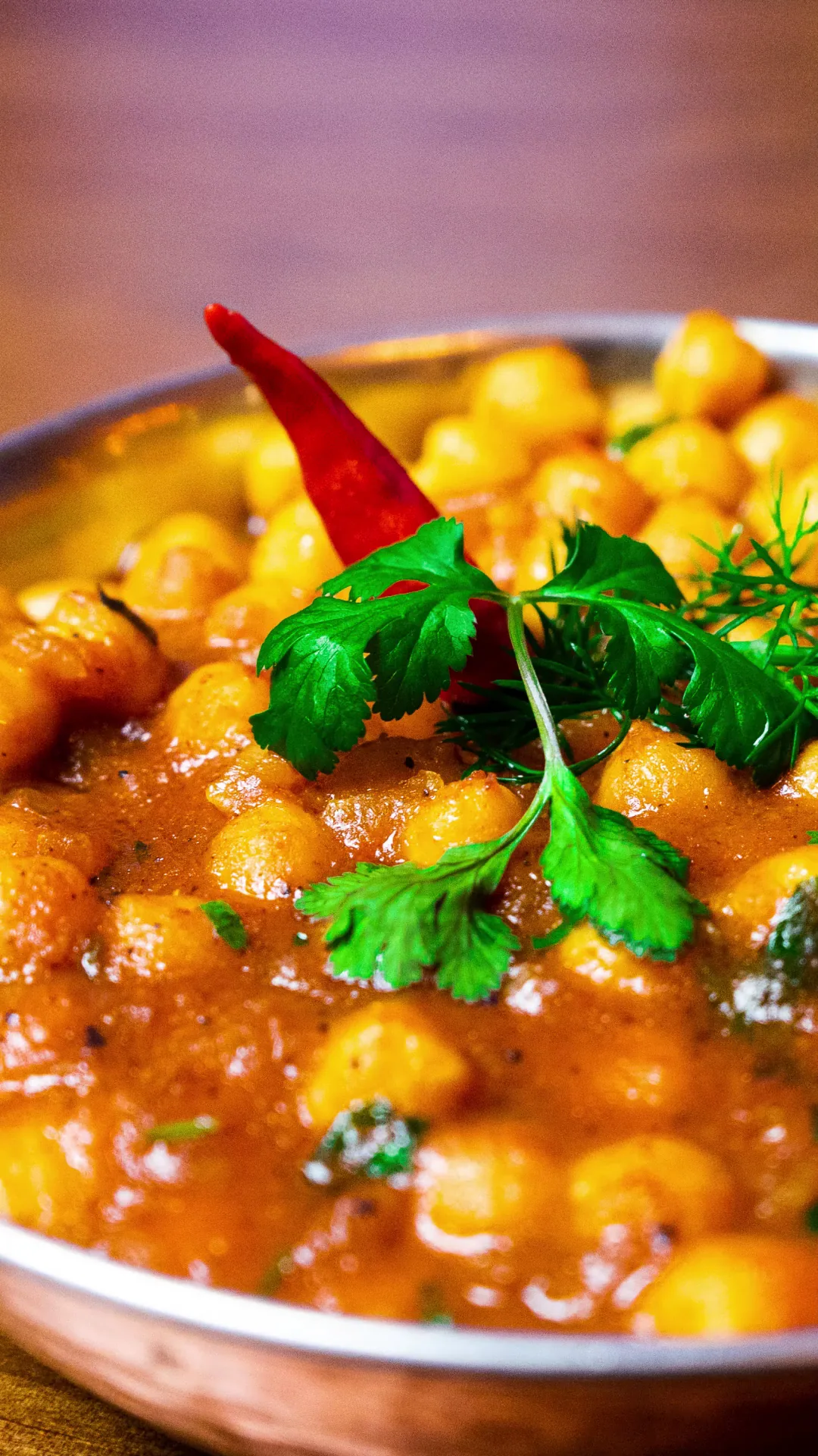 A copper bowl of chickpea curry garnished with fresh coriander and chili