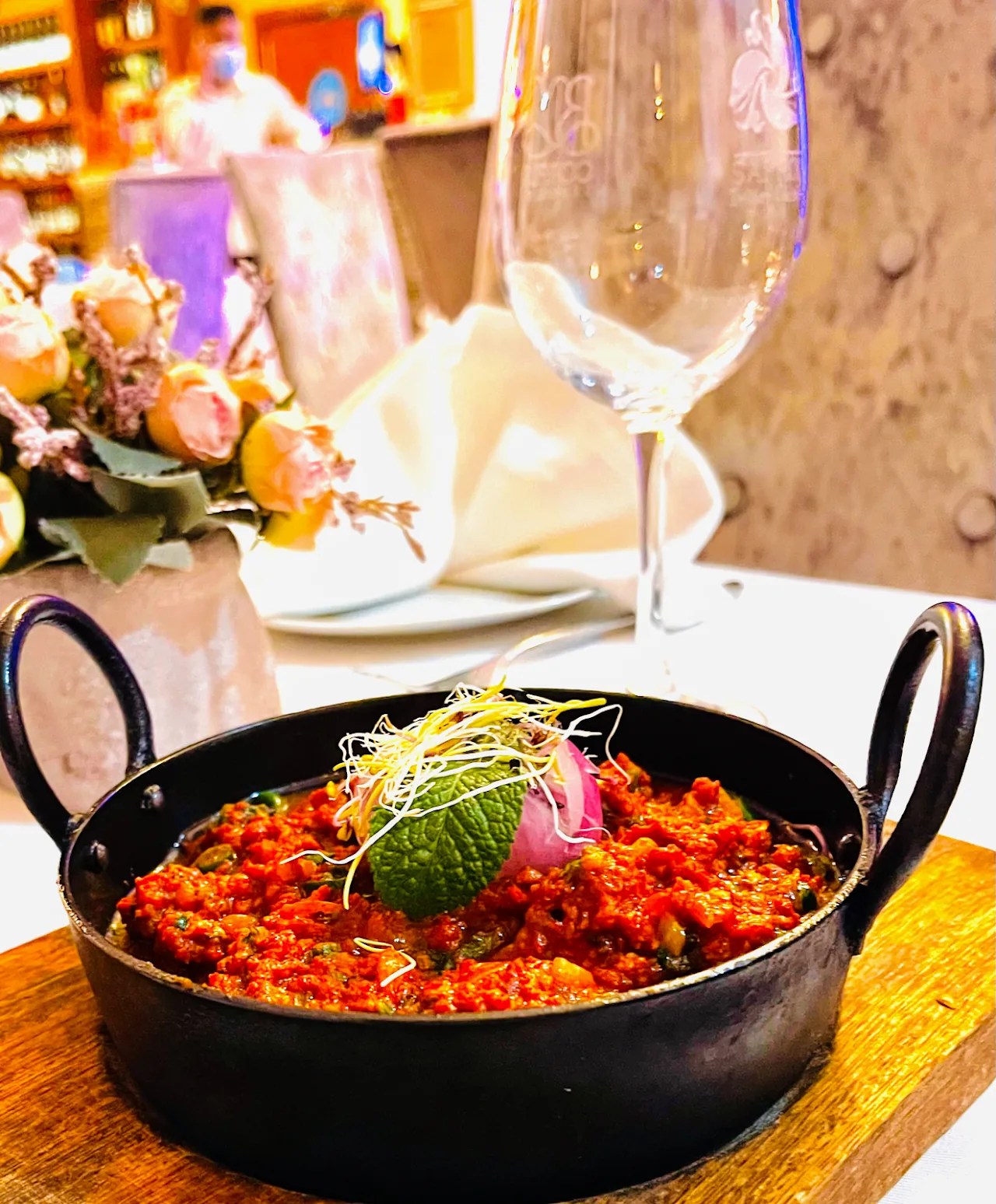 A black karahi of spiced curry served tableside with wine