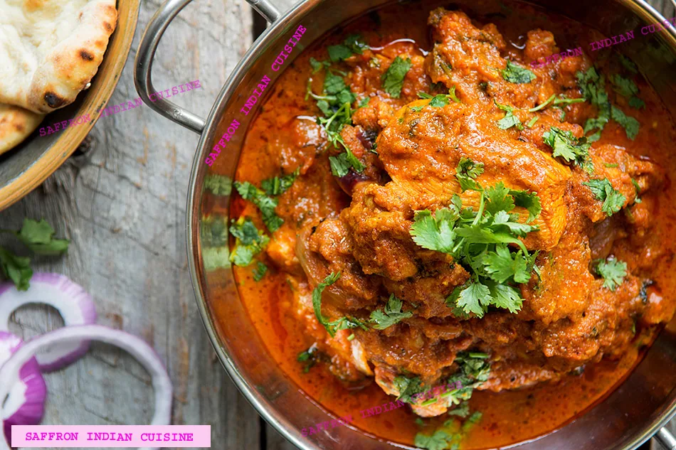 A bowl of chicken curry garnished with cilantro, served with naan