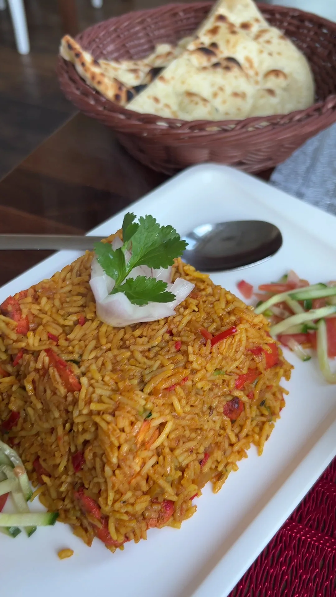 A wedge of biryani rice served with a basket of naan bread