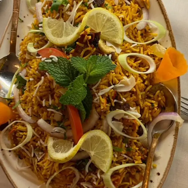 Oval platter of yellow biryani rice garnished with lemon slices, fresh mint, sliced onion rings and tomato