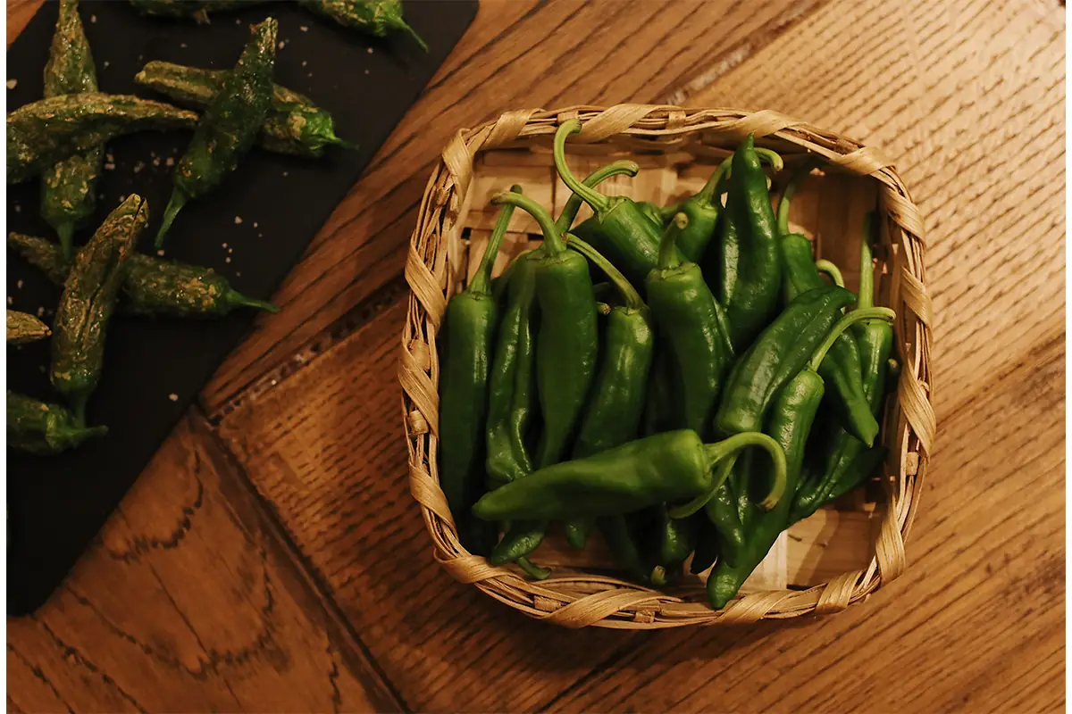 Fried Padrón-style green peppers with sea salt in a woven basket beside more on a slate board, Sagardi Argenteria