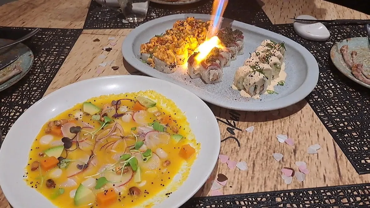 A table spread at Sakura Maru: ceviche in yellow leche de tigre with avocado, sweet potato and radish in front, and behind it maki rolls being finished with a blowtorch, flame still visible