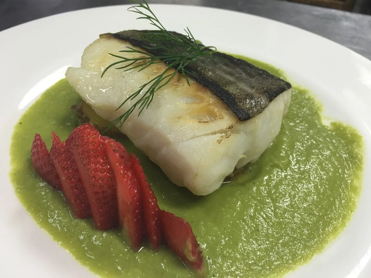 Grilled fish fillet over green sauce with roasted strawberries