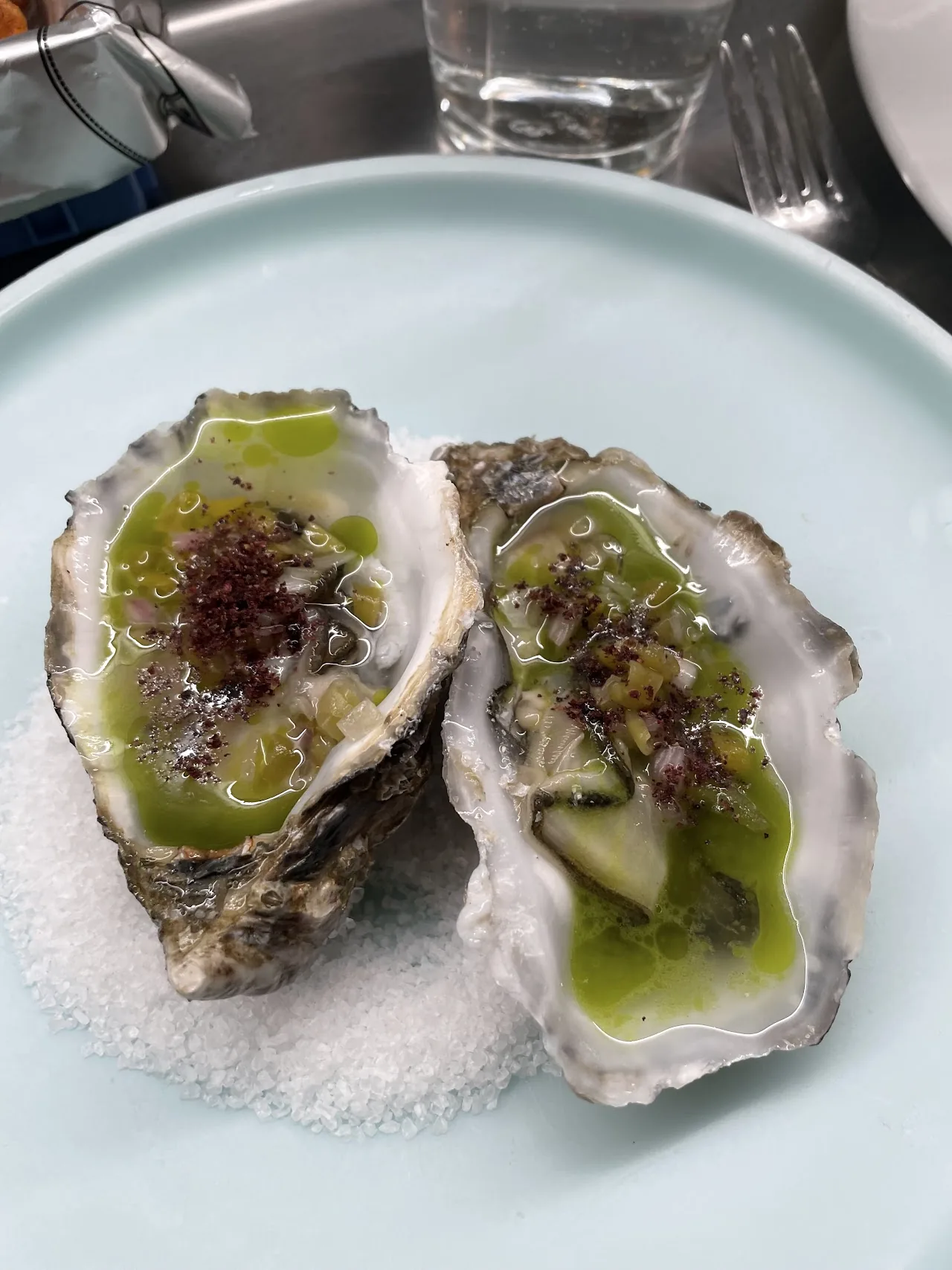 Two oysters on the half shell topped with a green herb sauce, served on salt