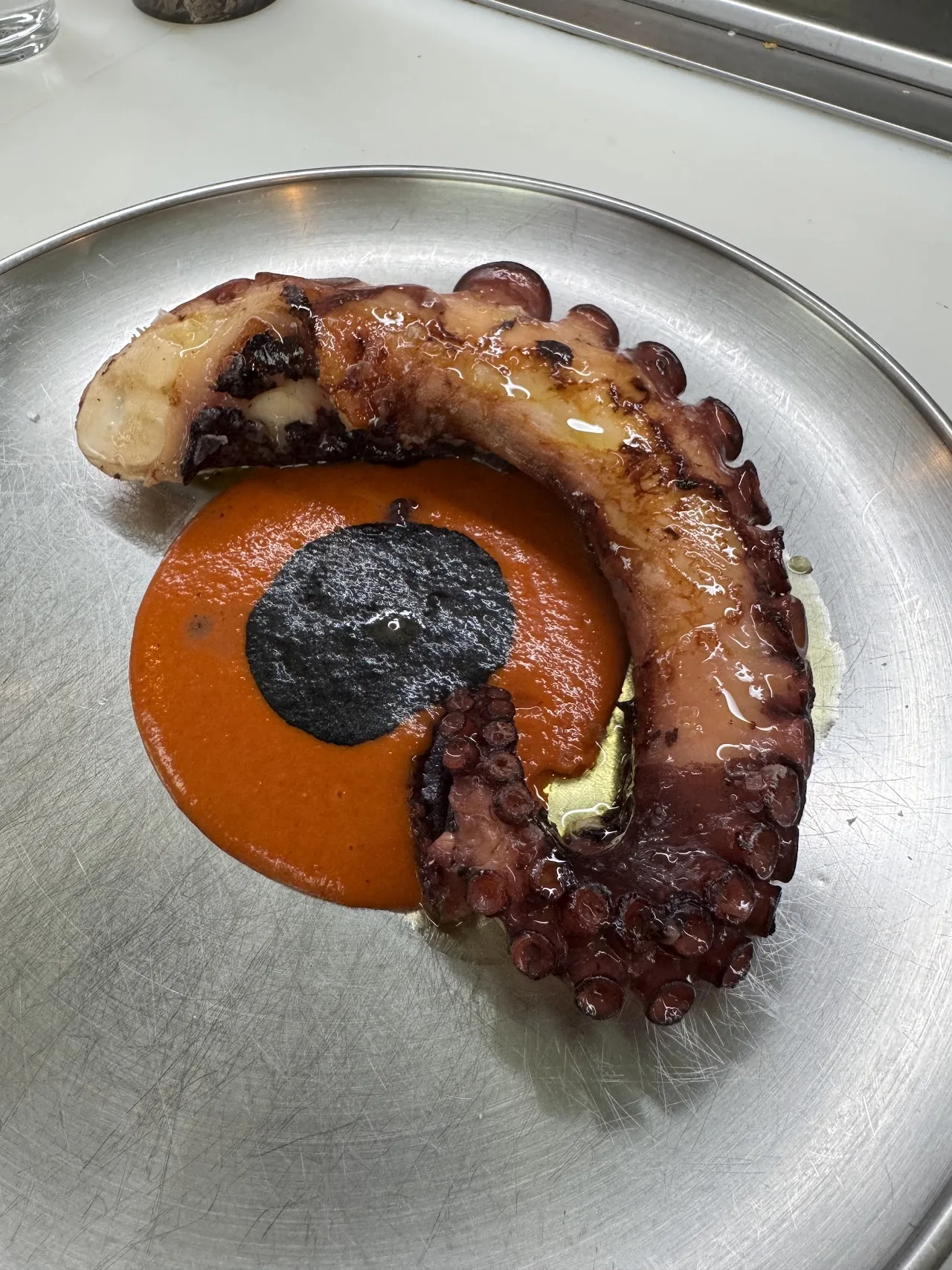 A curled grilled octopus tentacle plated with an orange sauce and dark garnish