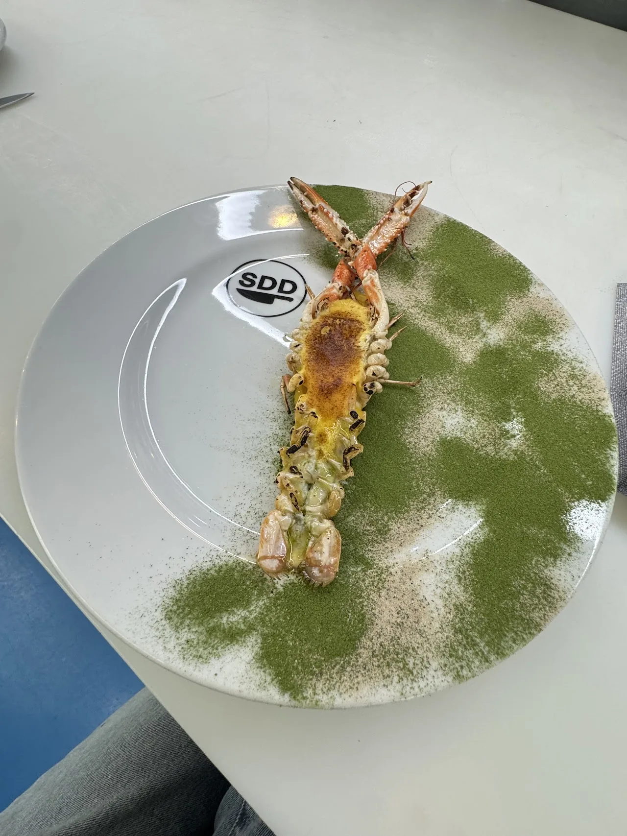 A whole grilled shrimp dusted with green herb powder on a plate