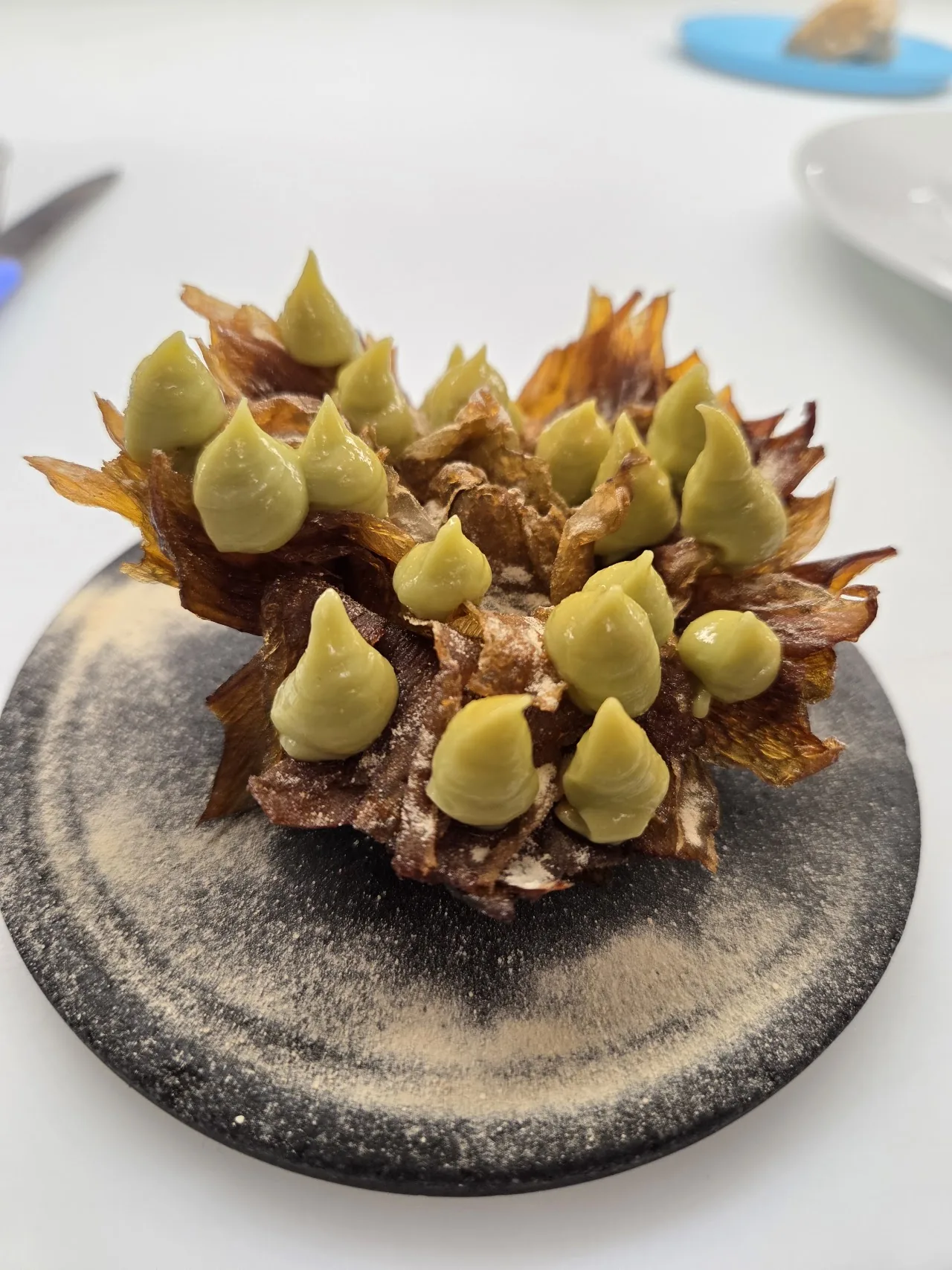 A plated dish of charred baby artichokes with green sauce dots