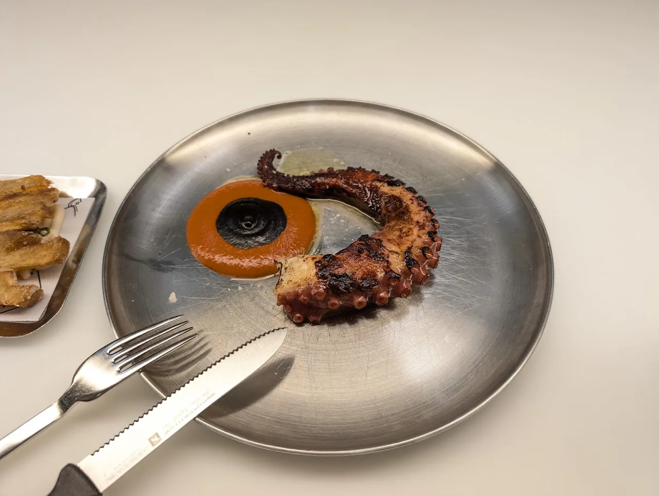 A curled octopus tentacle on a plate with orange romesco-style sauce and toasted bread