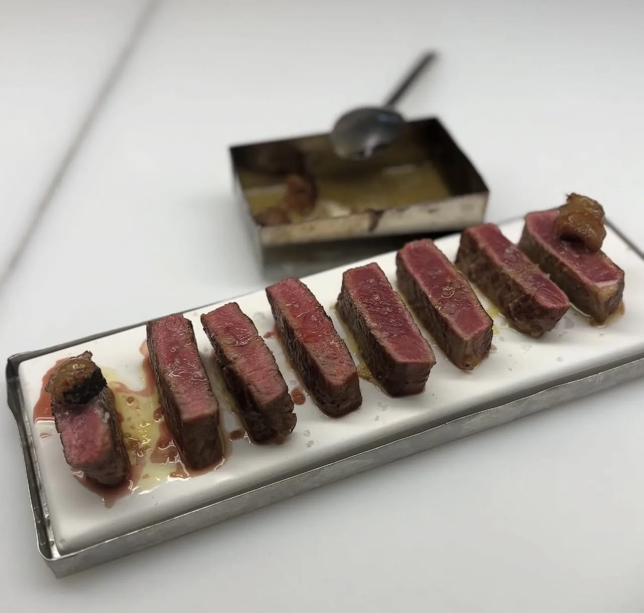 A row of sliced seared beef tenderloin on a metal tray
