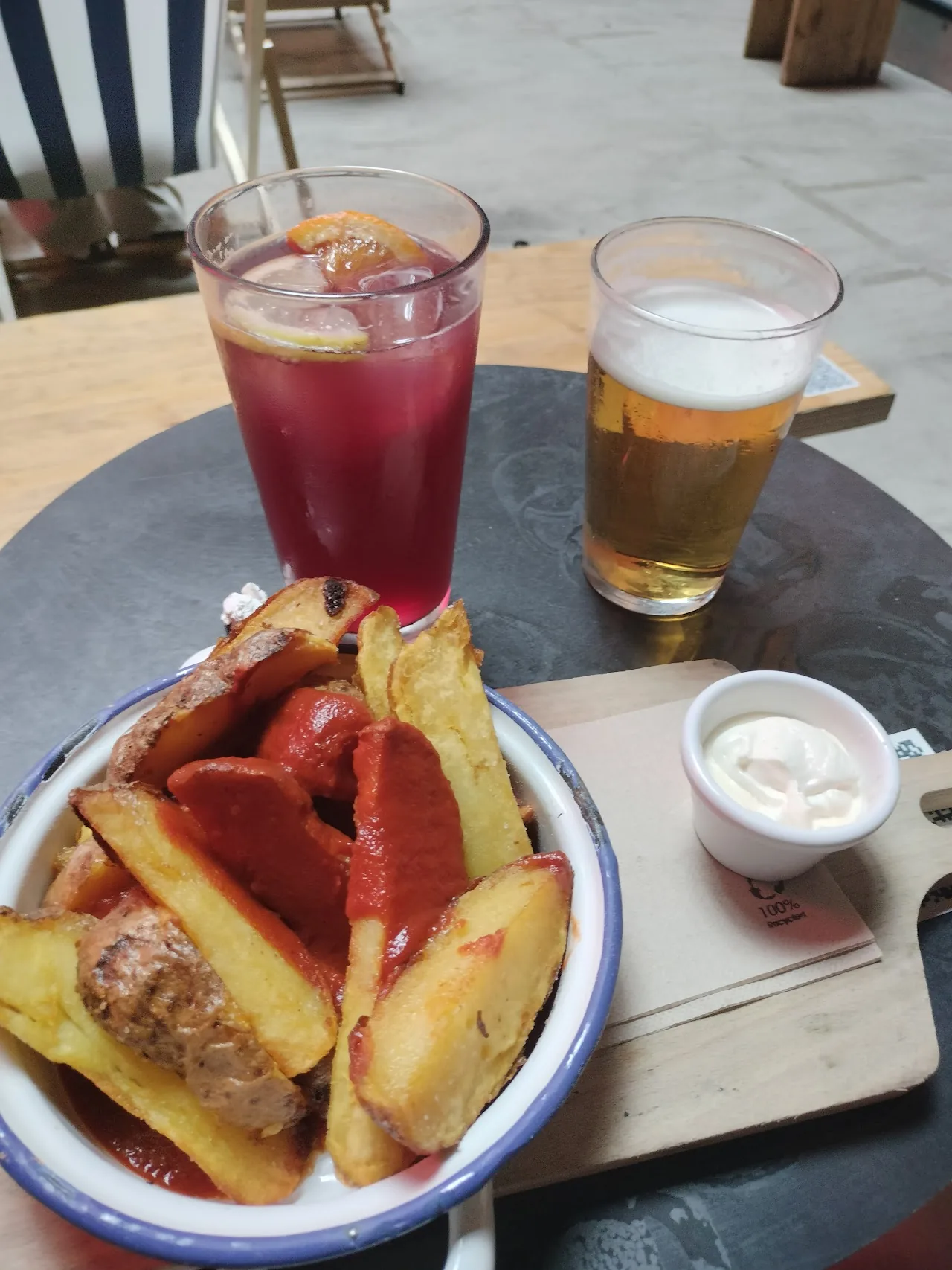 A plate of fries with grilled sausage and a dip, next to drinks