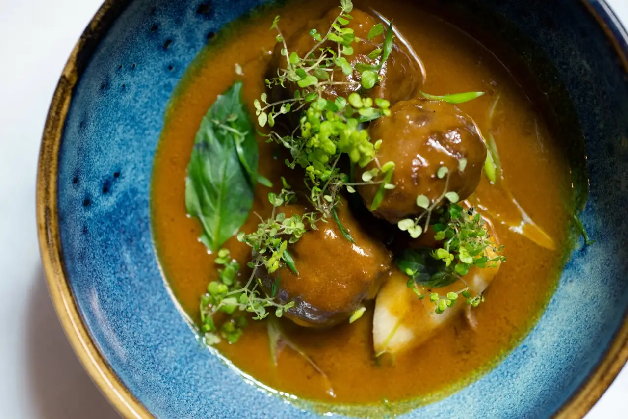 Overhead shot of glazed meatballs in brown sauce topped with microgreens and basil in a blue-rimmed ceramic bowl