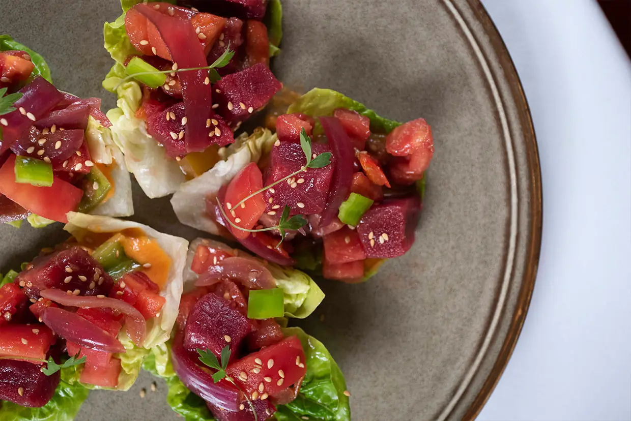 Tuna tartare and diced tomato served in little gem lettuce cups sprinkled with sesame seeds on a stoneware plate
