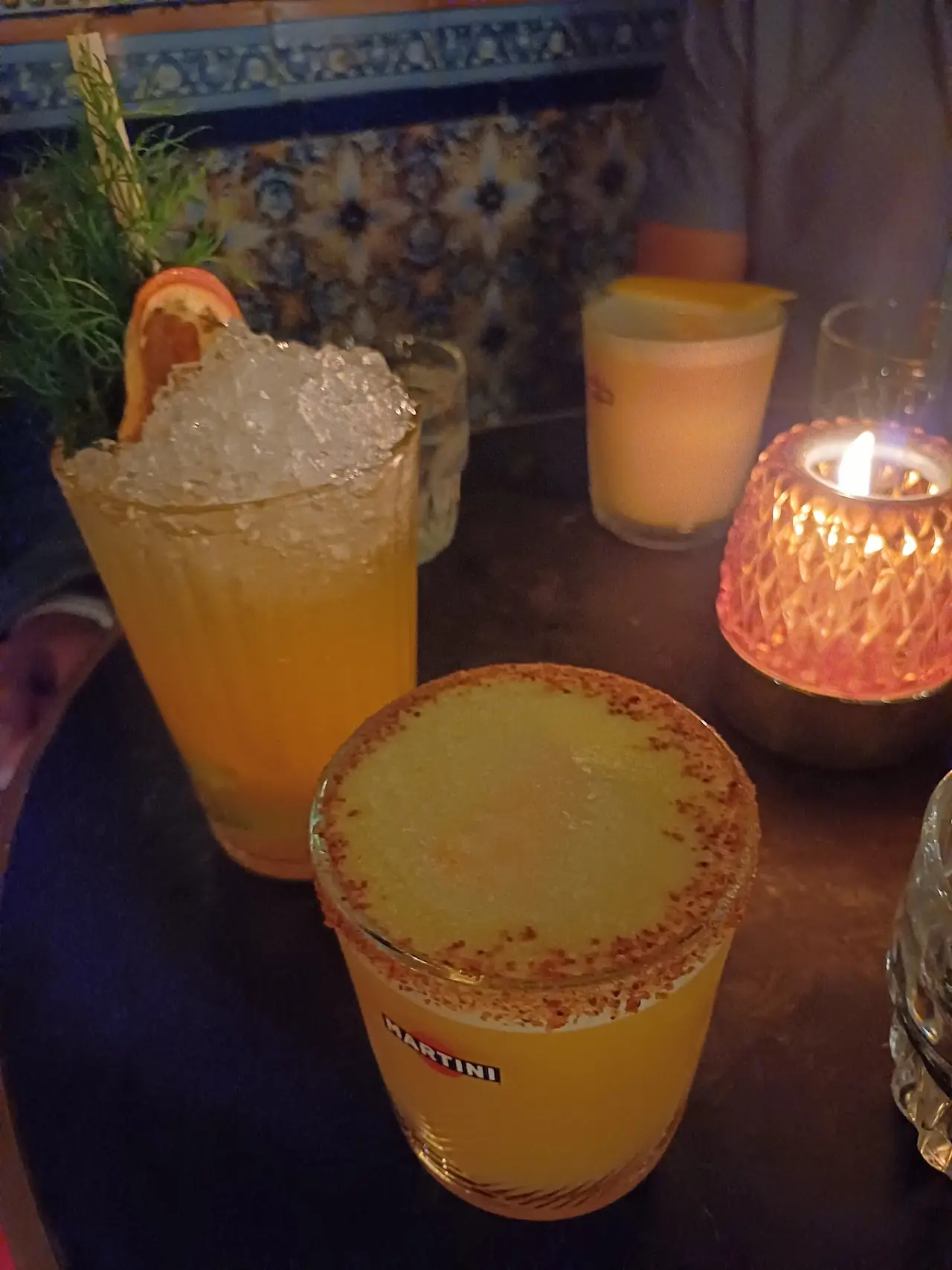 Two orange cocktails with spiced-salt rims on a candlelit table.