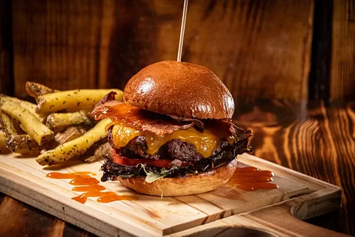 Smash burger with melted cheddar, crispy bacon, and seasoned wedge fries on a wooden board, Samambahia Restaurante & Cachaça Bar