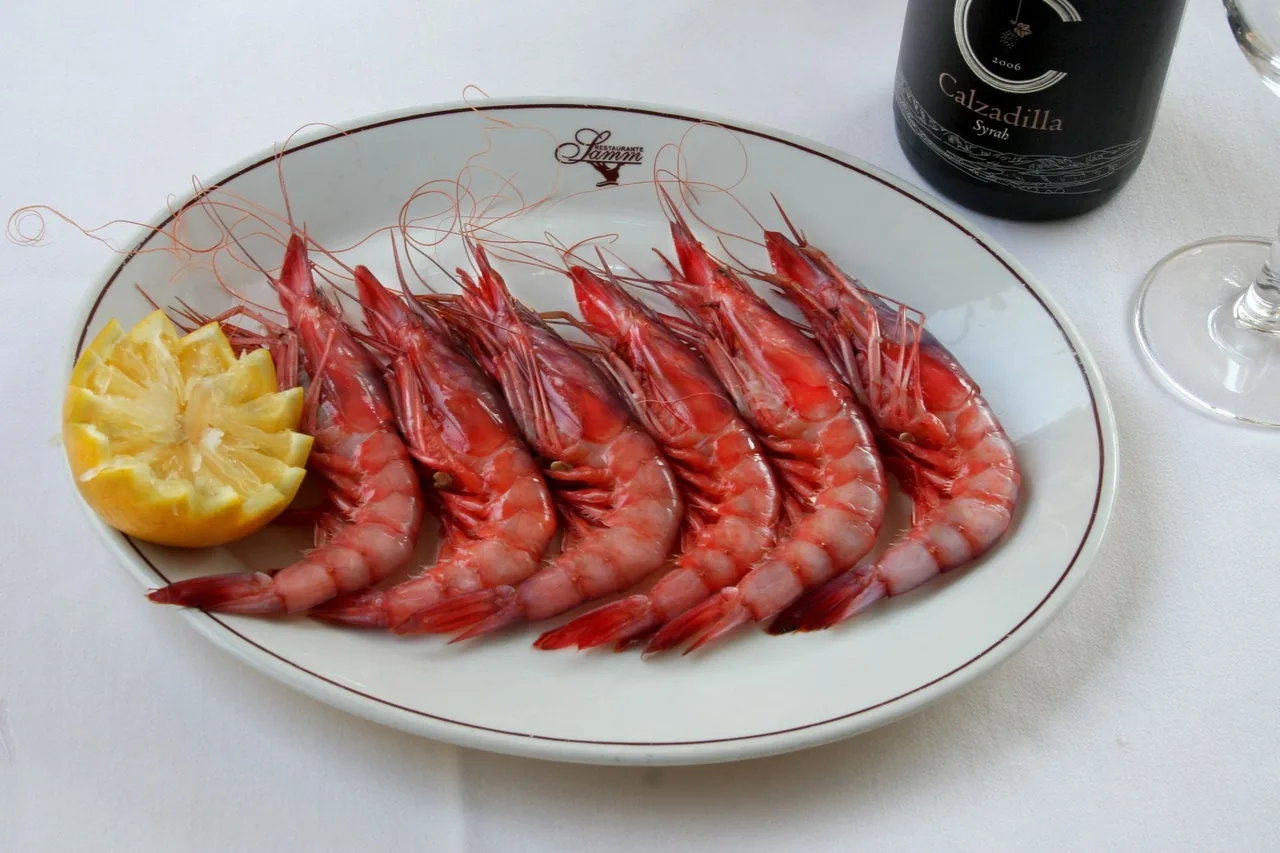 A row of whole red prawns with a lemon half on a white plate