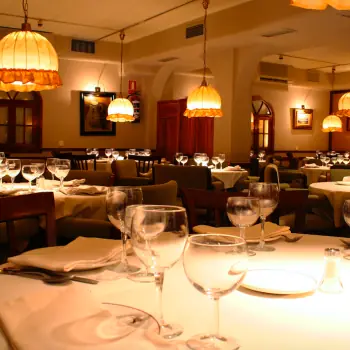 Dining room with wood-paneled walls, framed artwork, and tables set with wine glasses under hanging lamps