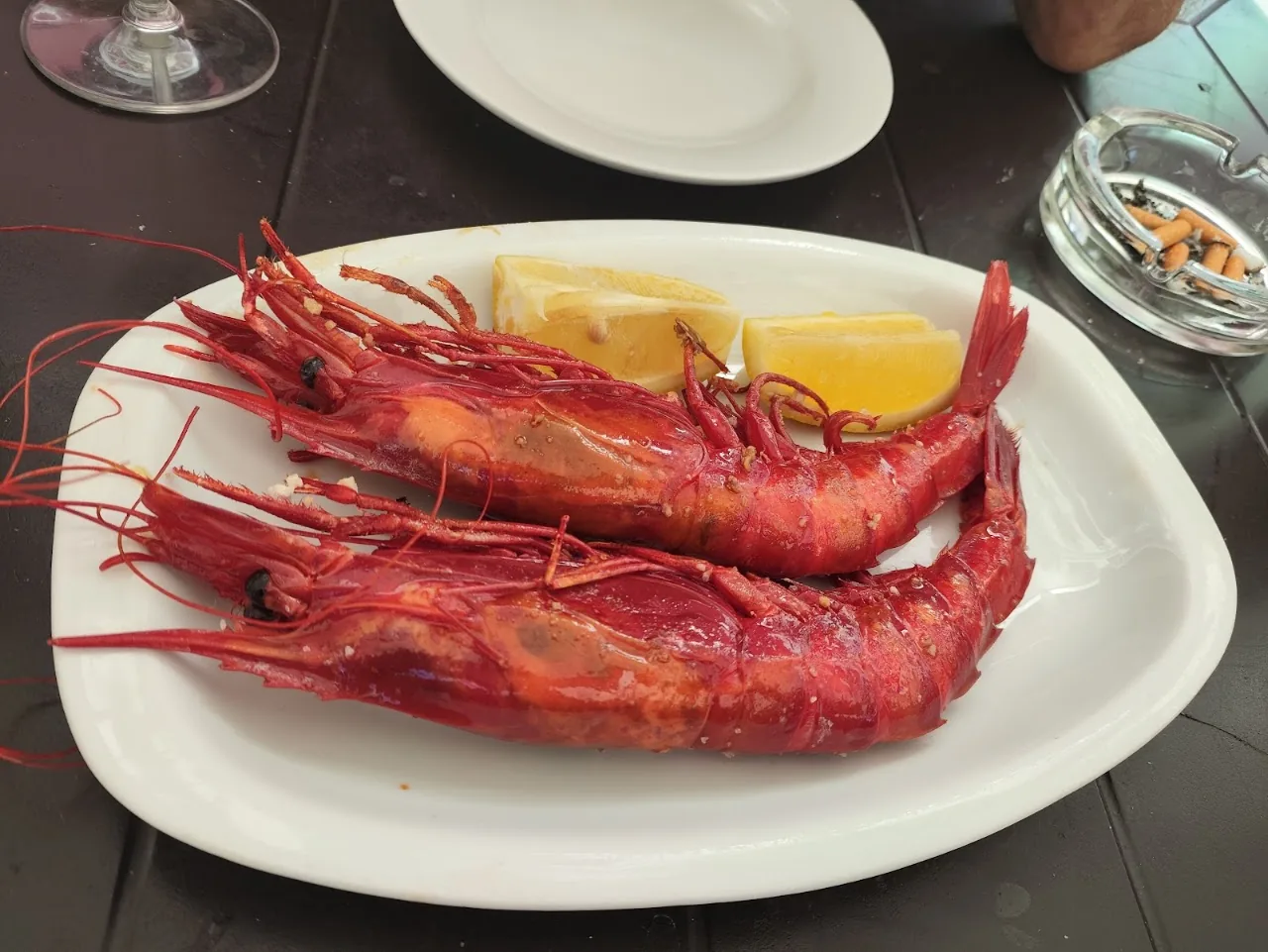 Two whole grilled red prawns on a plate with lemon
