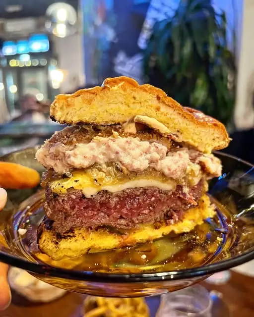 Cross-section of a thick burger showing a rare patty, melted cheese and toppings on a brioche bun, on a glass plate