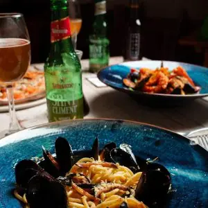 Spaghetti with mussels in a blue bowl, with another seafood pasta dish and drinks in the background at Santa Clara