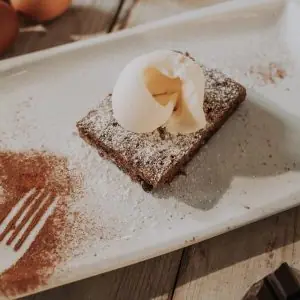 Chocolate brownie dusted with cocoa and powdered sugar, topped with a quenelle of cream, on a white plate at Santa Clara