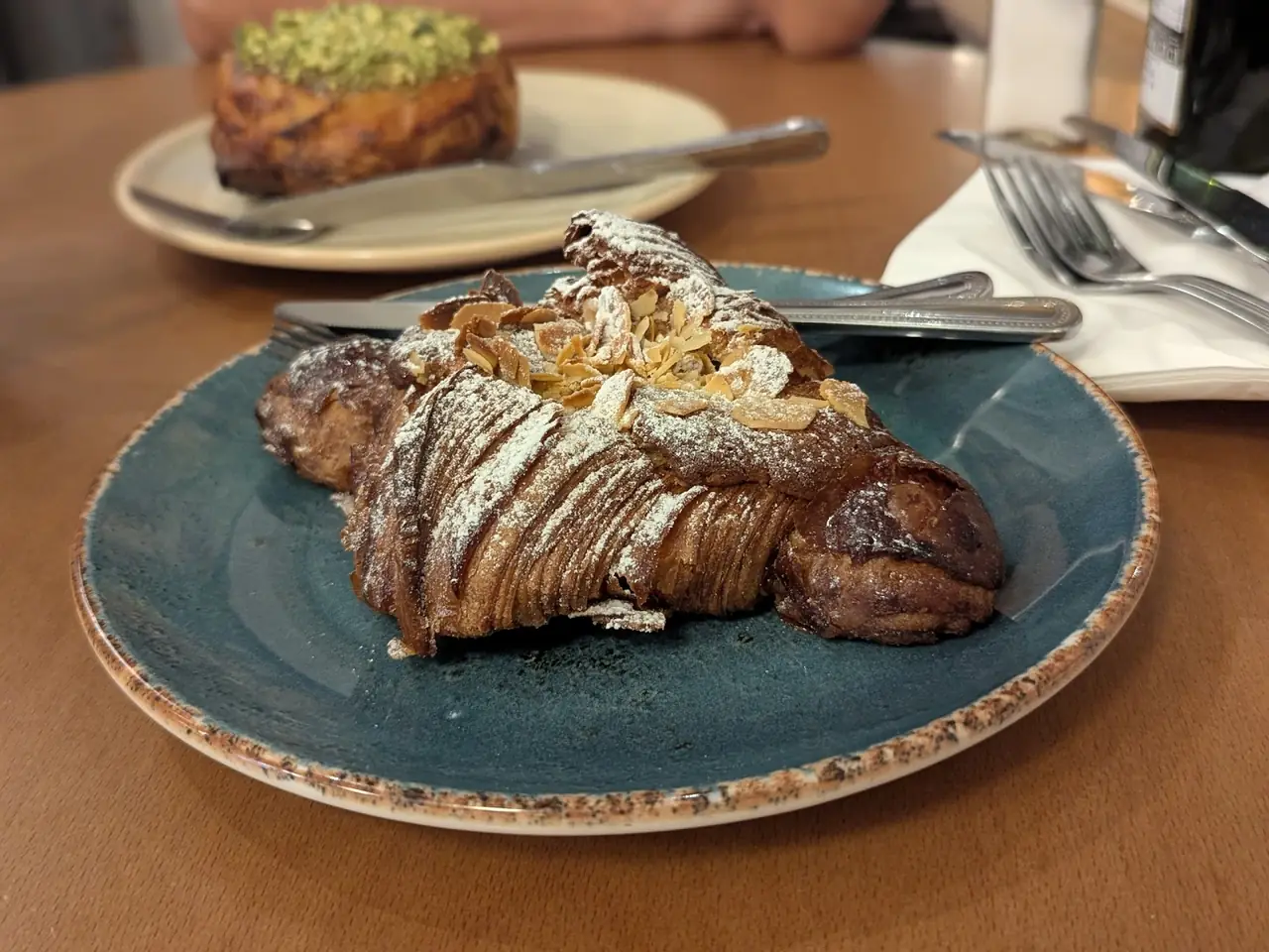 Almond croissant dusted with powdered sugar and topped with sliced almonds, on a plate