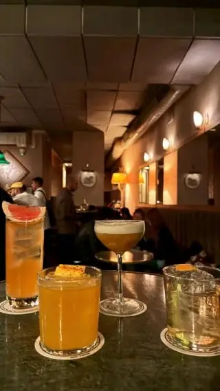 Three cocktails on coasters on a dark bar table in a dimly lit lounge with wall sconces