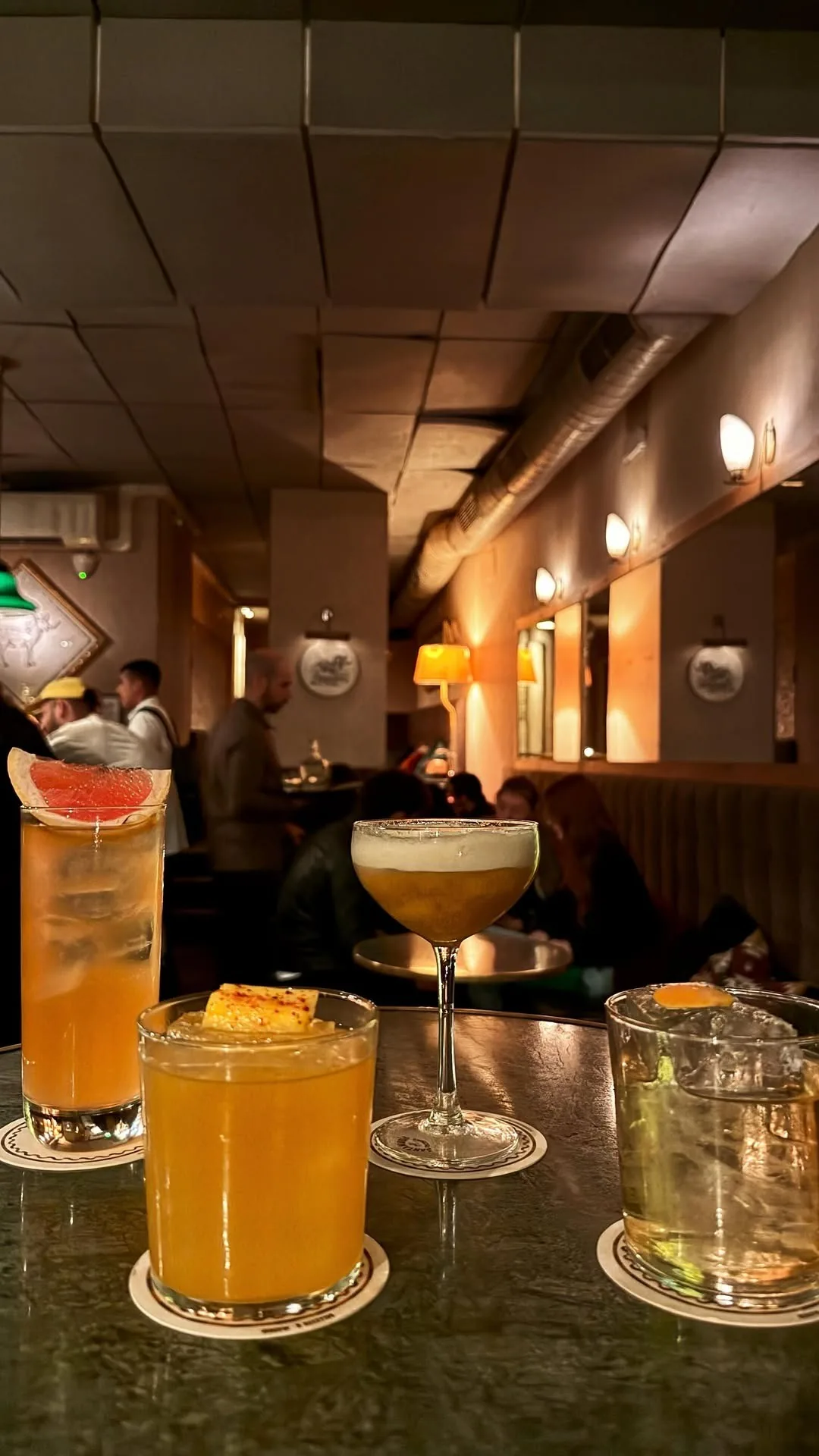 Several cocktails in different glasses lined up on a dark bar counter