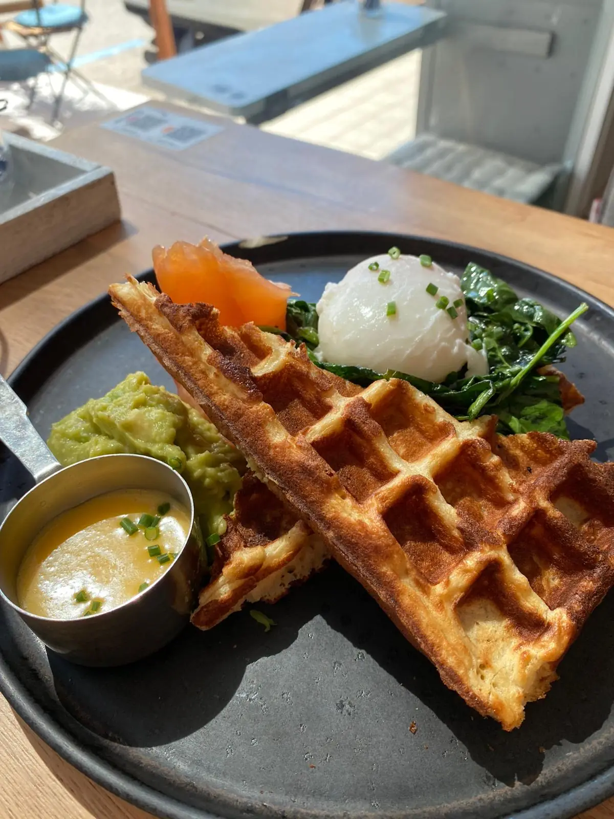 Waffle with poached egg and greens next to a small cup of soup