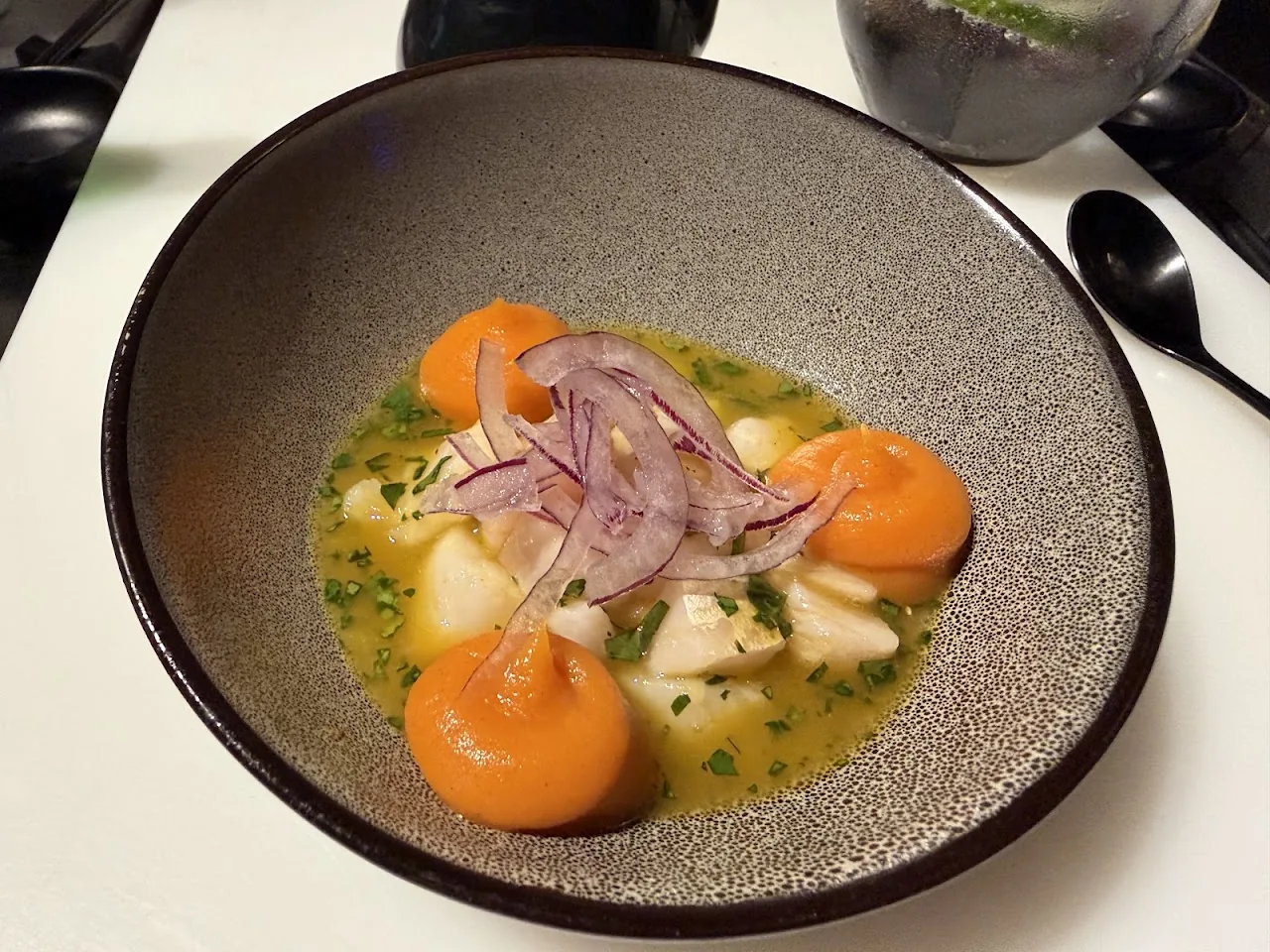 A bowl of scallops with orange segments and pickled onion in broth