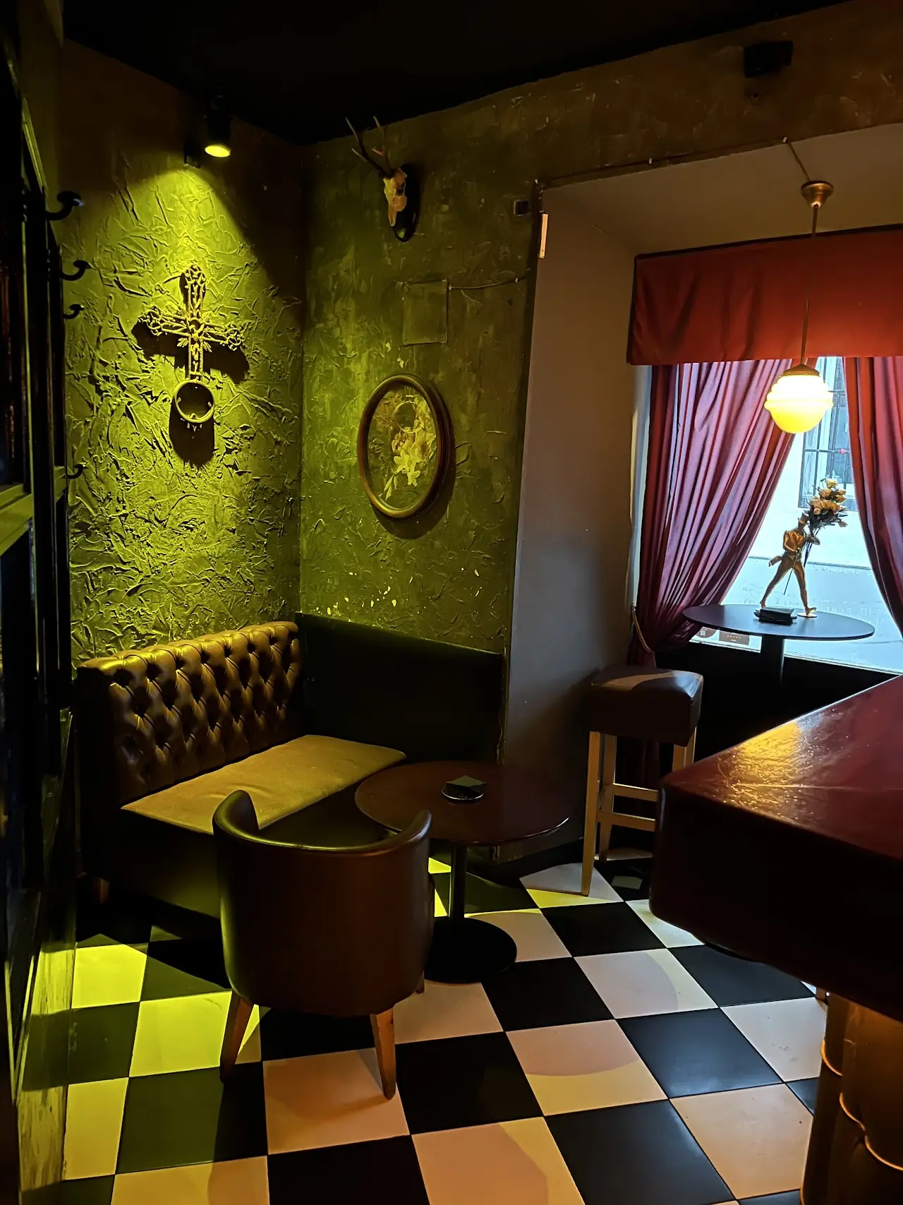 A corner of the bar with green textured walls, a checkerboard floor and leather seating