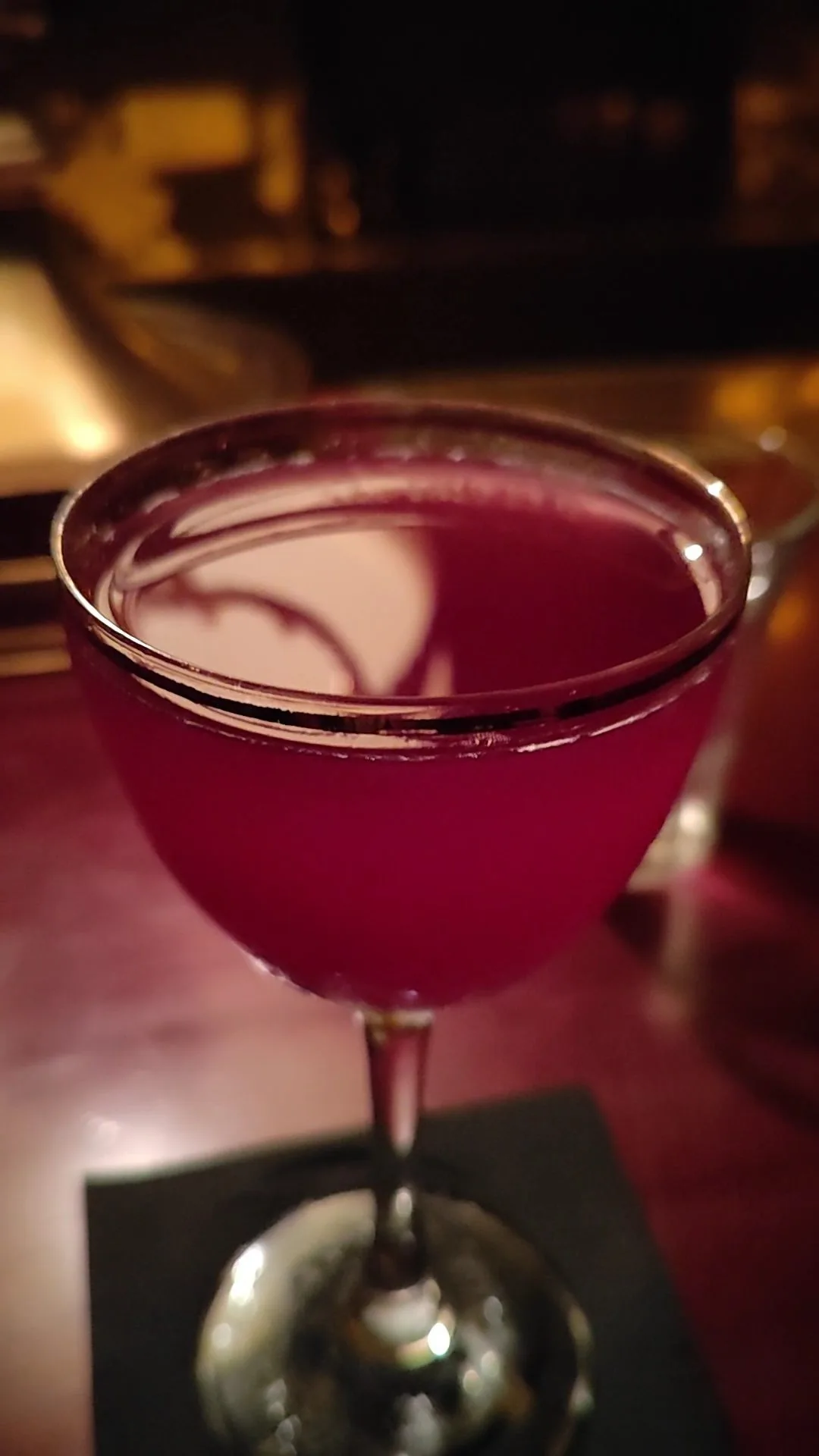 A pink cocktail in a coupe glass on a coaster